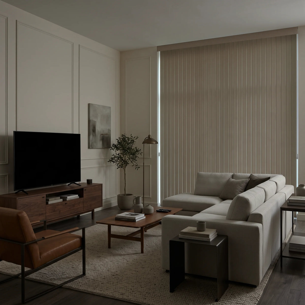 A modern living room featuring a large beige Vertical Blinds covering a window, styled with a light gray sectional sofa, a dark wood media console with a television, a brown leather armchair, and a low wooden coffee table on a textured rug.