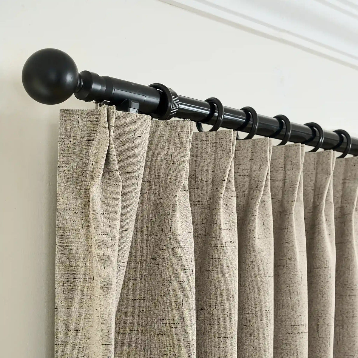 Curtain rod with beige curtains against a white wall