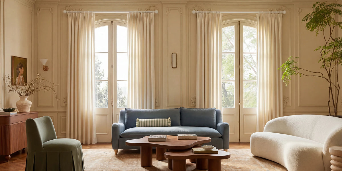 Modern living room with a blue sofa, white armchair, large curtain and wooden coffee table.