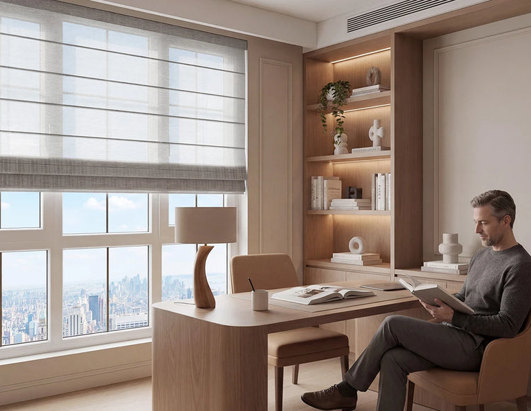 Man sitting at a desk in a modern office with large windows shades and bookshelves.