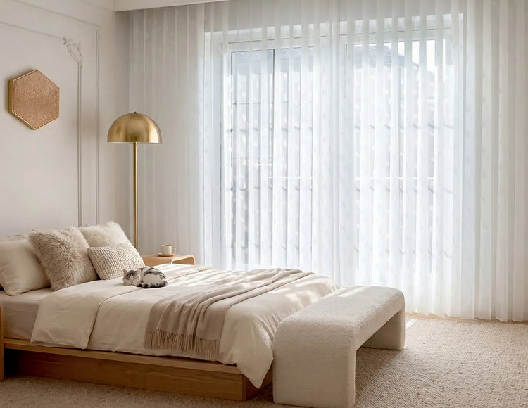 Modern bedroom with a bed, lamp, and large window with sheer vertical blinds.