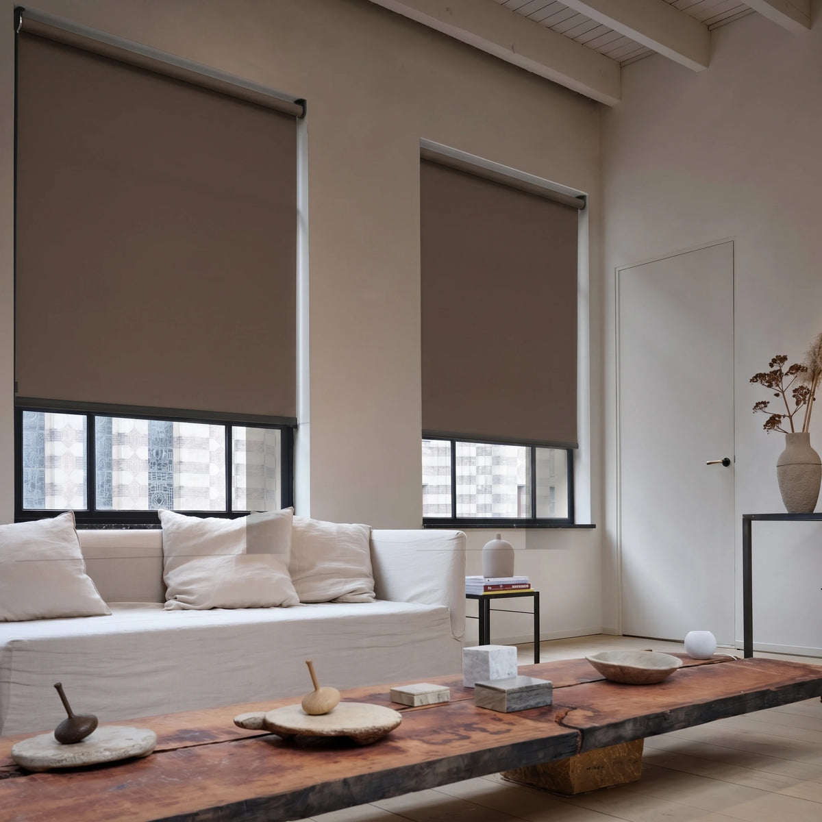 Modern living room with beige roller shades, a wooden coffee table, and a sofa with white pillows.