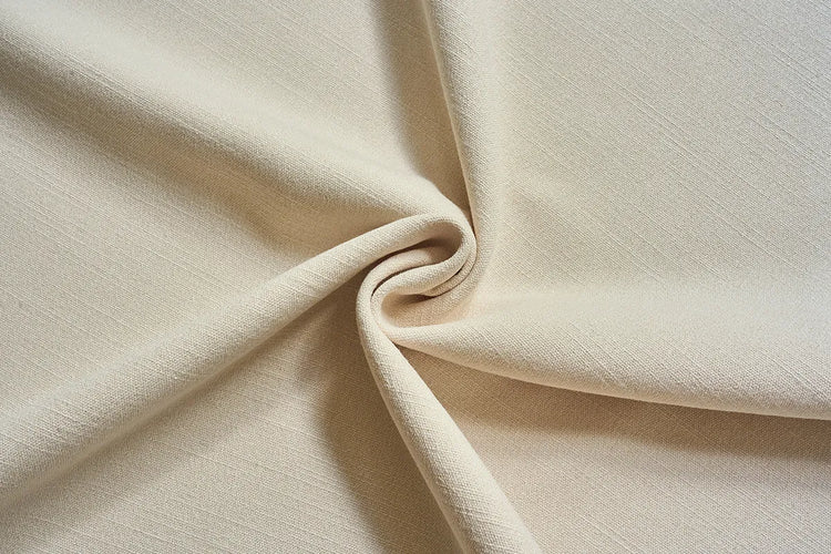 A close-up of draped cream-colored fabric with a soft, textured weave, arranged in elegant folds and a central swirl.