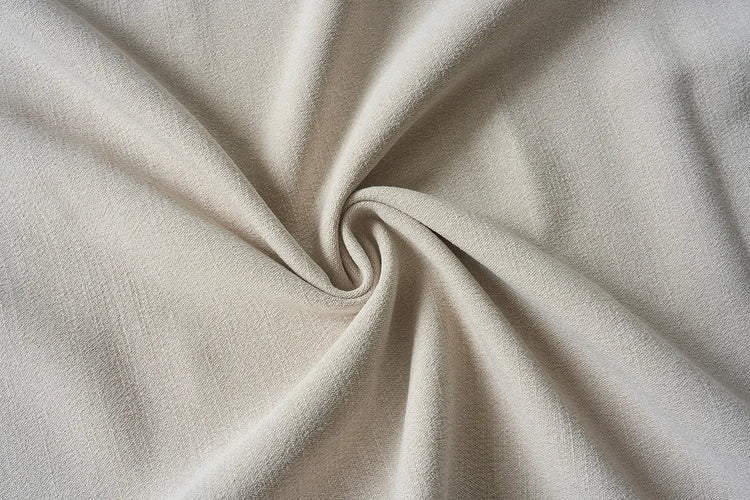 A close-up of draped off-white fabric with a central swirl, showing its soft texture and light neutral color.