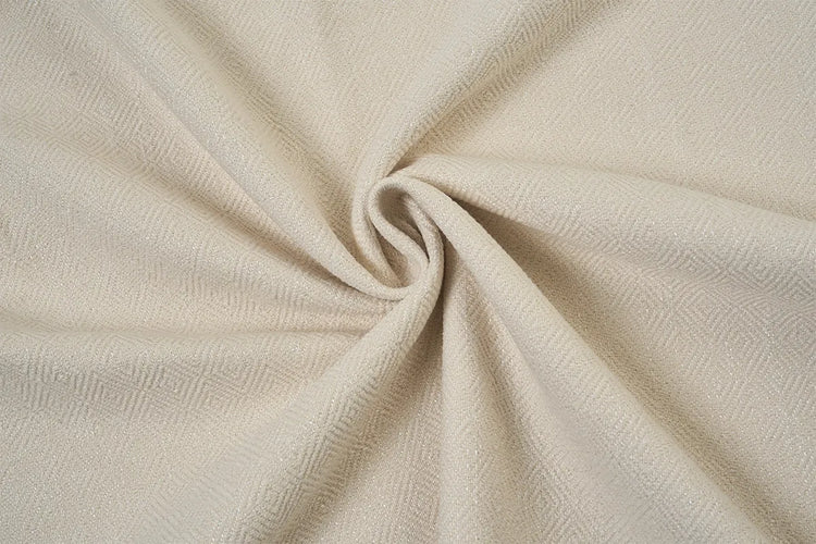 A close-up of textured cream-colored fabric arranged in a spiral drape, showing its woven pattern and soft folds.