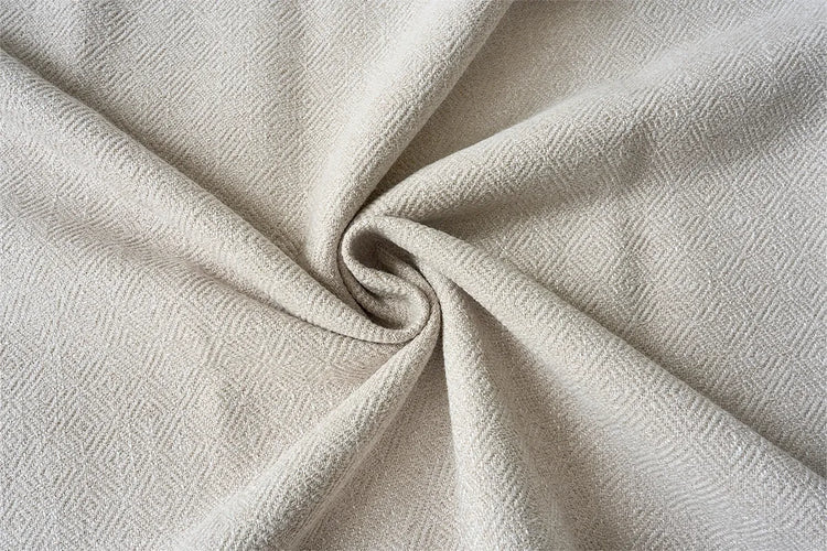 A close-up of draped fabric with a subtle woven texture, shown in soft folds and swirls. The material appears in a warm off-white or light beige tone.