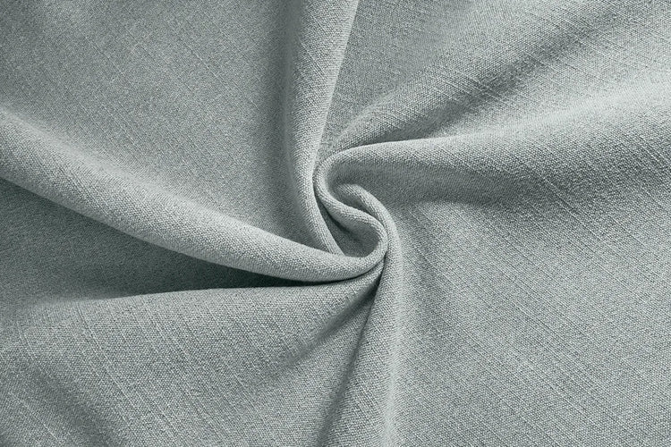 A close-up of light blue-gray textured fabric arranged in a spiral drape, showing the material's fine weave and soft folds.