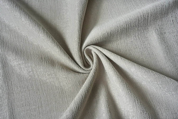 A close-up of draped light beige fabric with a subtle woven texture, arranged in a spiral pattern.
