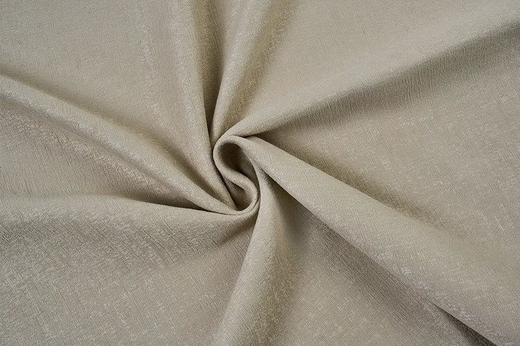 A close-up of draped fabric in a warm light beige or taupe color, arranged in a spiral fold to show texture and drape.