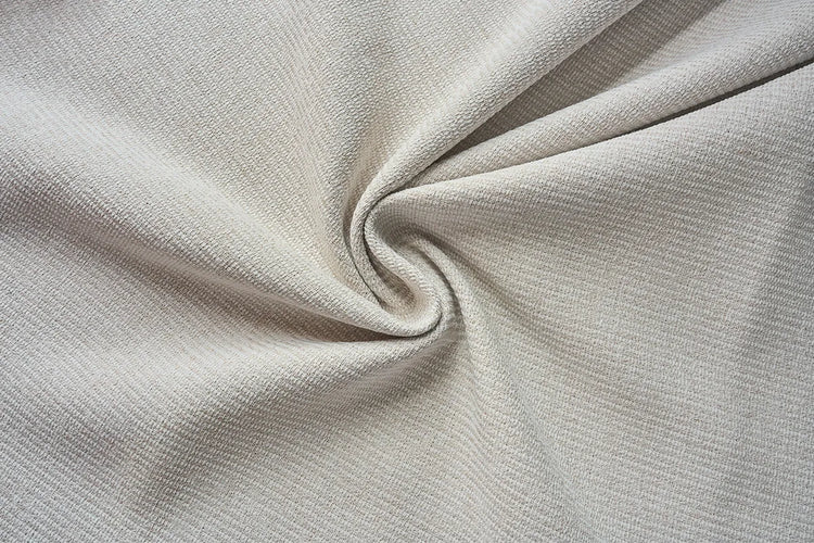 A close-up of light beige textured fabric with soft folds and a central swirl, showing the material's fine woven pattern.