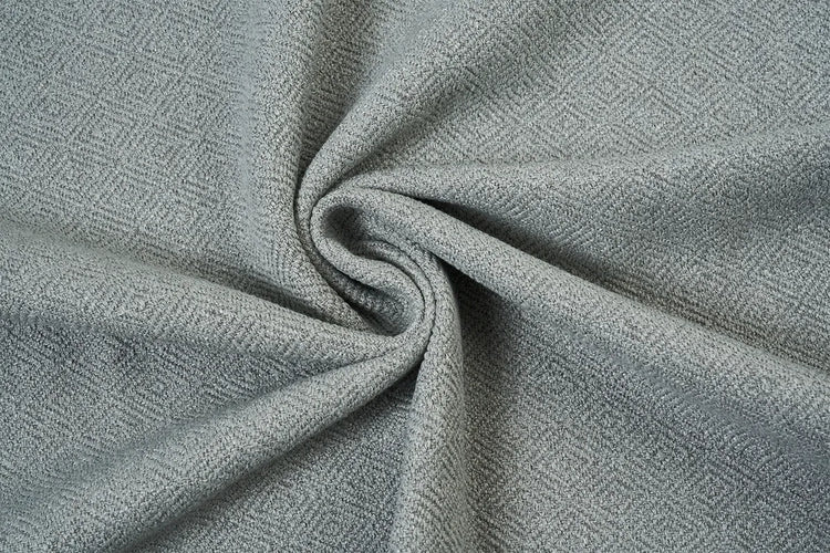 A close-up of textured fabric with a fine herringbone pattern in light gray and white, arranged in a spiral drape.