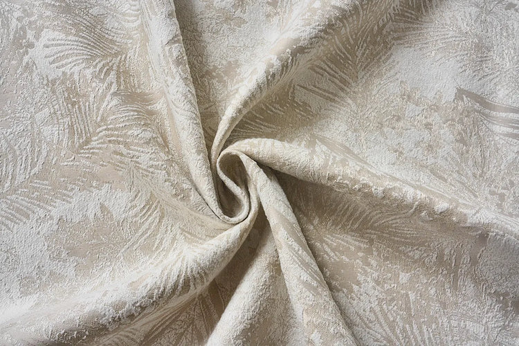 A close-up of draped fabric with a subtle woven leaf or feather-like pattern in warm ivory and beige tones.