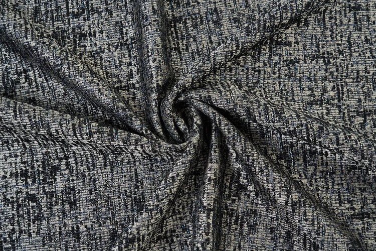 A close-up of a textured fabric with a heathered, woven pattern in black, gray, and white, arranged in a central swirl to highlight its drape and texture.
