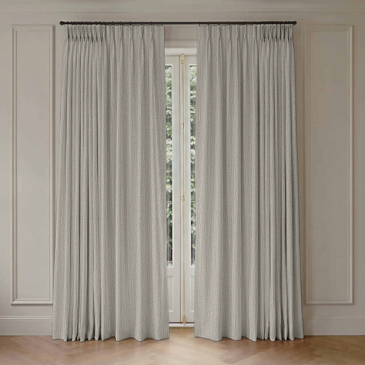A pair of light gray textured window curtains hanging from a dark metal rod in a room with cream paneled walls and a light wood floor.