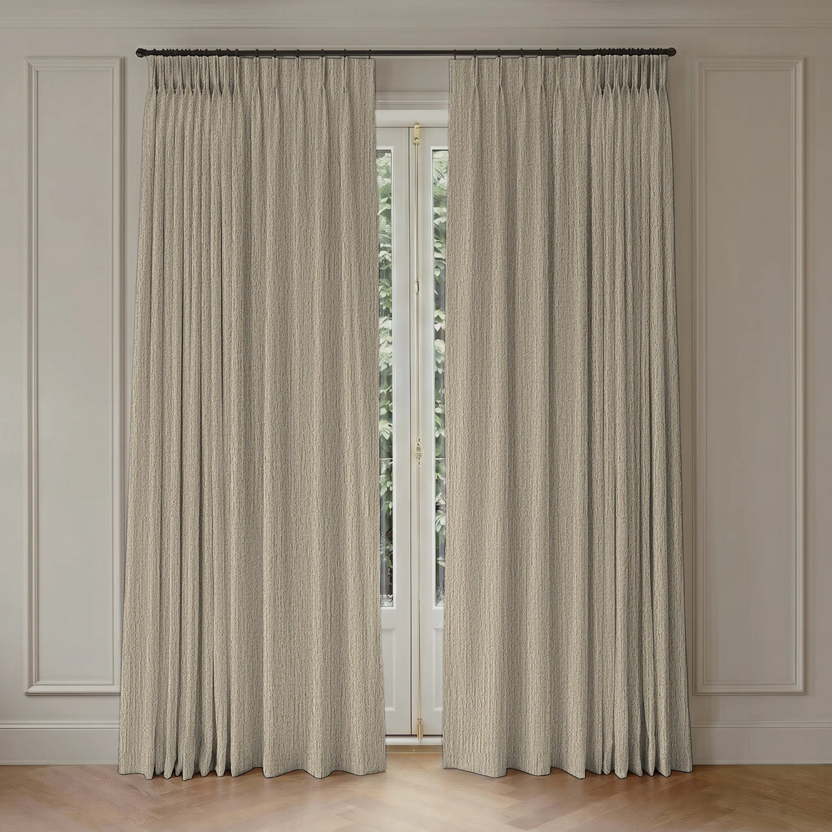 A pair of textured beige pleated window curtains hanging from a dark metal rod in a room with white paneled walls and a light wood floor.