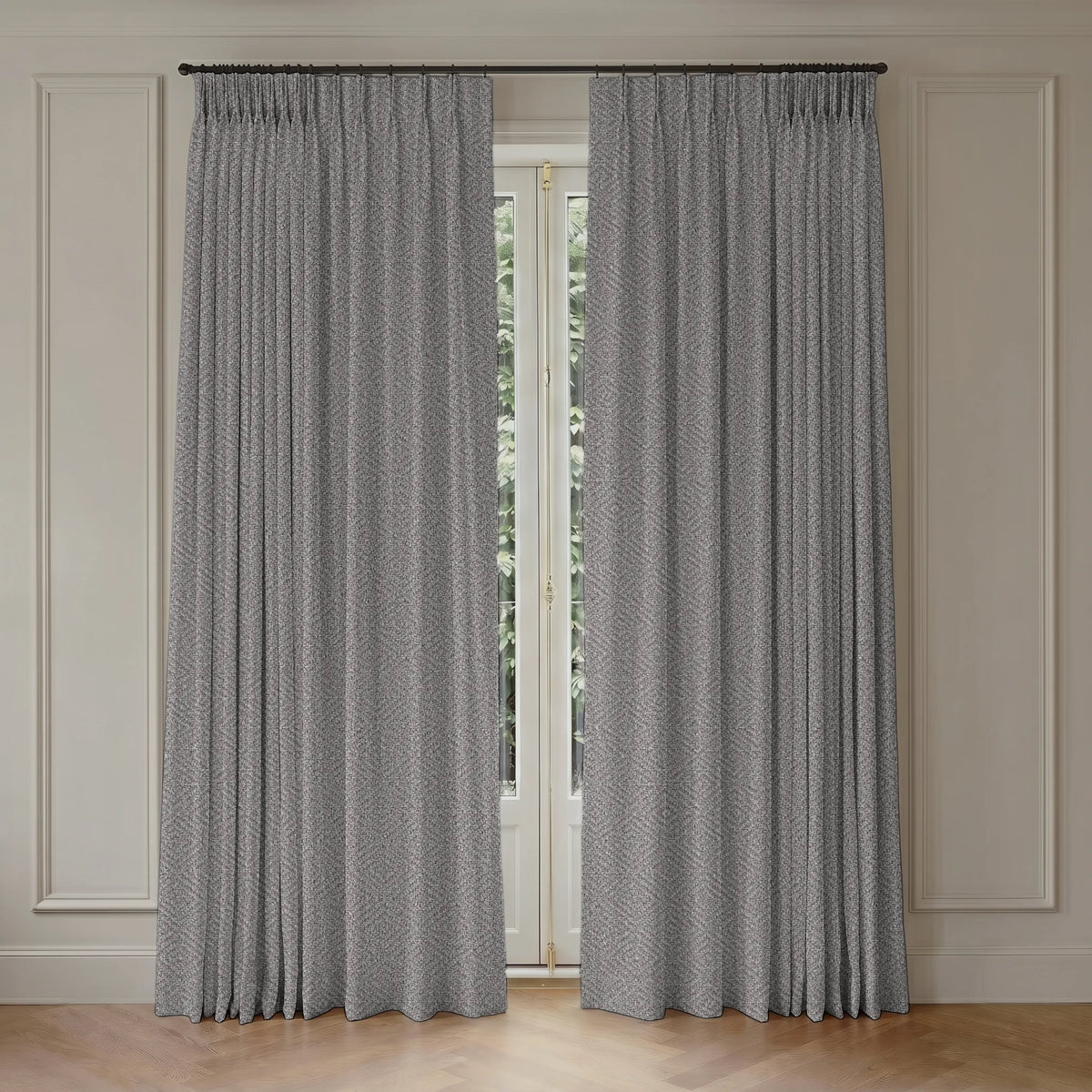 A pair of gray textured window curtains hanging from a black rod in a room with cream paneled walls and a light wood floor.