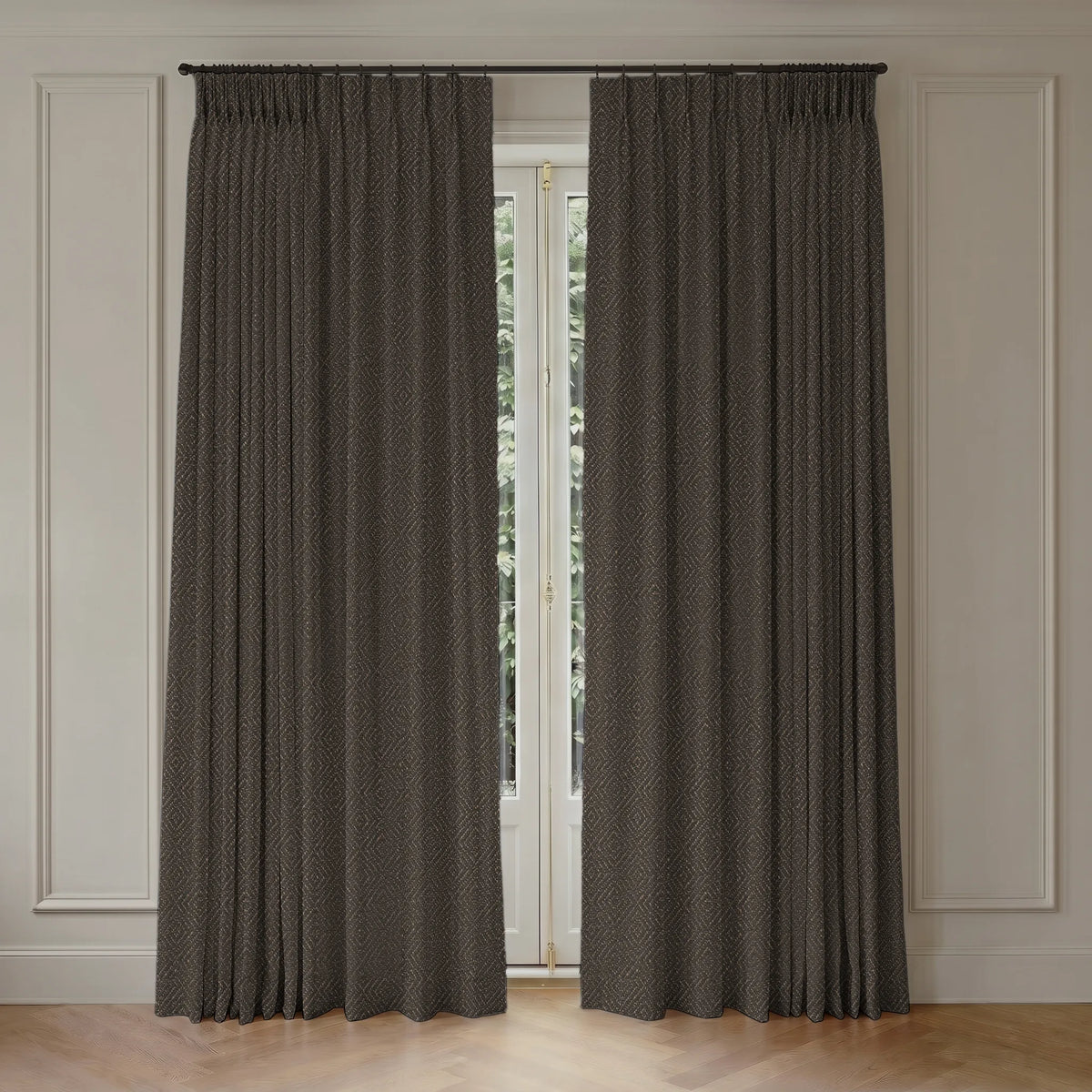 A pair of dark brown textured window curtains hanging on a black rod in a room with white paneled walls and a light wood floor.