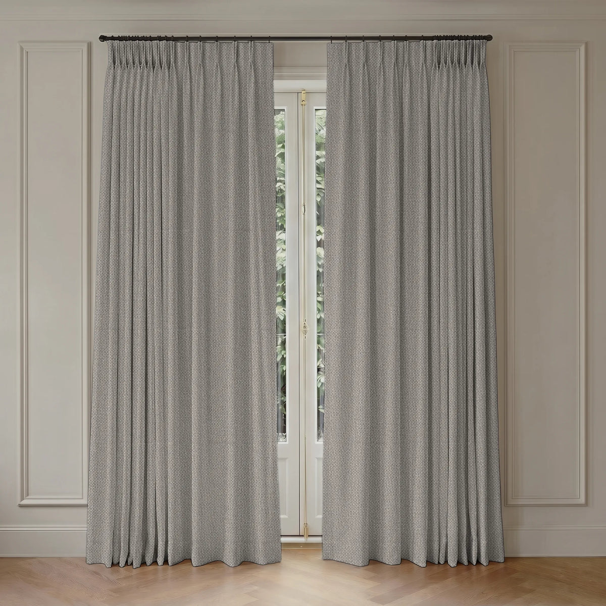 A pair of light gray textured window curtains hanging from a dark metal rod in a room with cream paneled walls and a light wood floor.