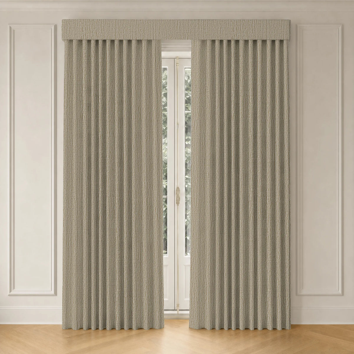 A pair of floor-length pleated curtains in a light beige textured fabric, hanging on a window in a bright room with white paneled walls and light wood flooring.