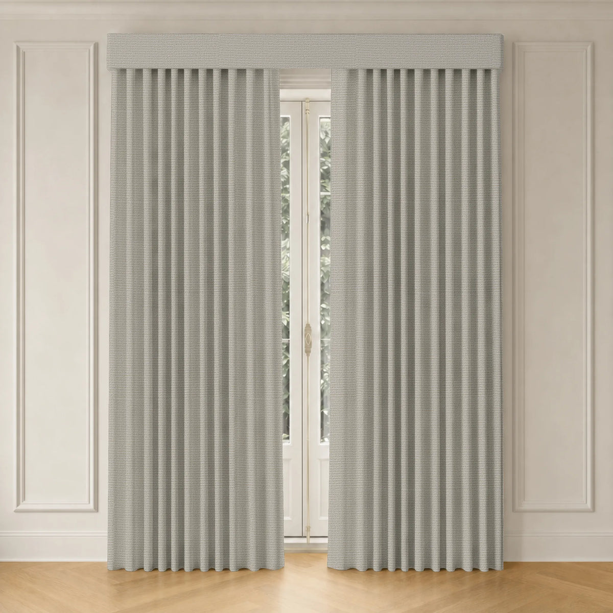 A pair of light gray pleated window curtains hanging on a rod in a bright room with white paneled walls and a light wood floor.