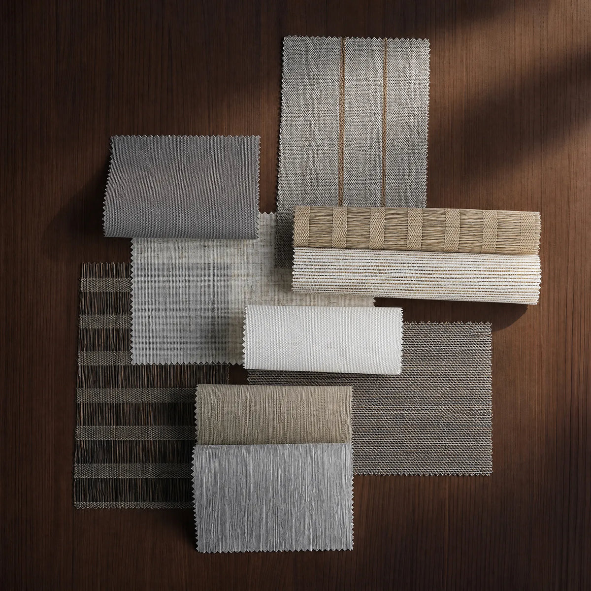 A collection of textured fabric and material swatches in neutral tones, including gray, beige, brown, and white, arranged on a dark wood background.