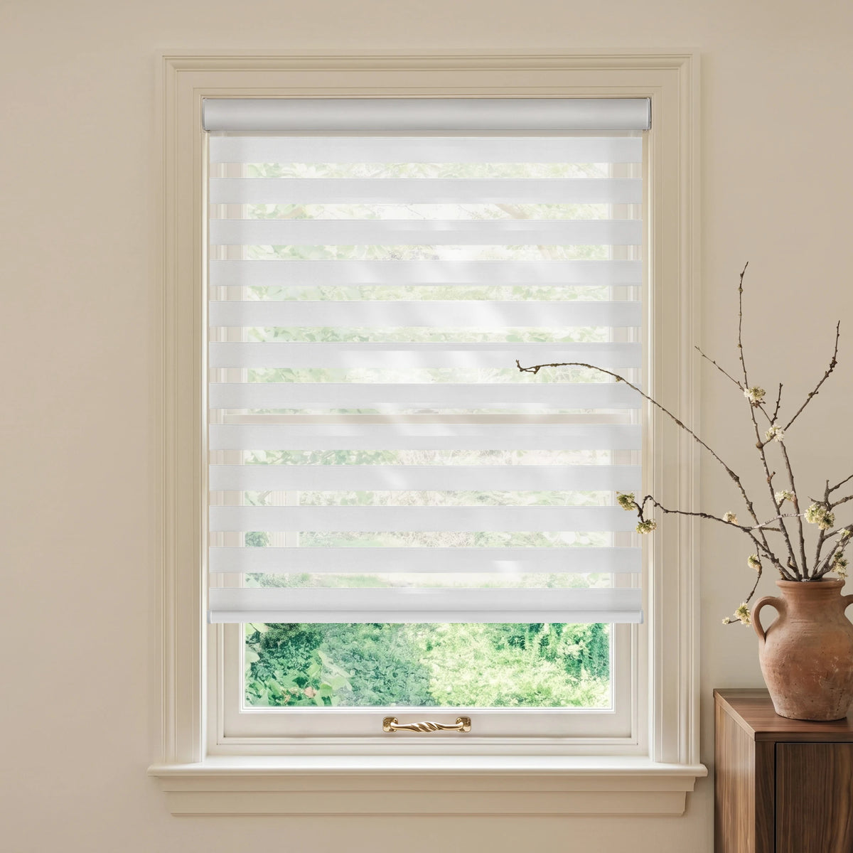 Fire Retardant White motorized light-filtering zebra blind with green trees outside and a terracotta vase nearby.