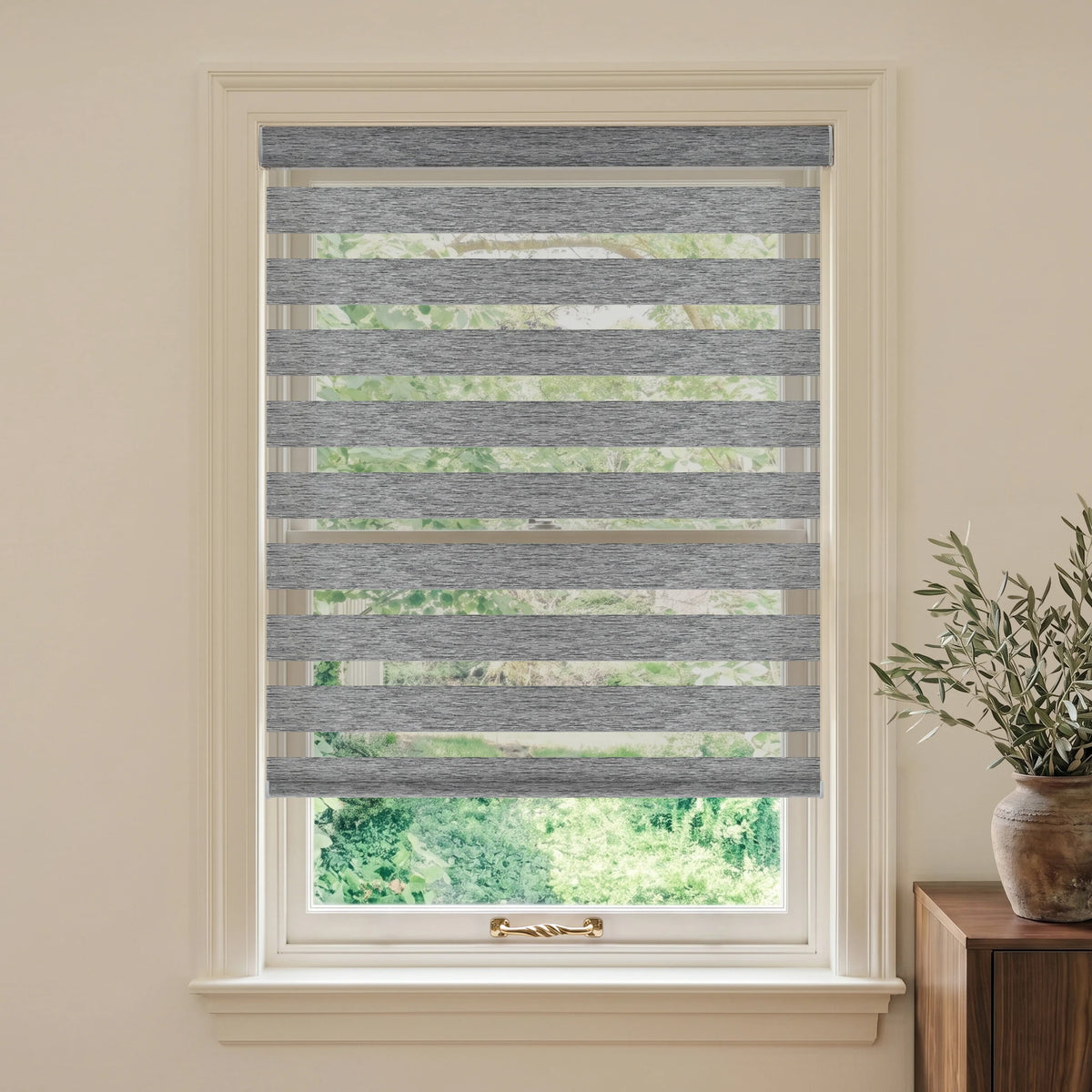 Bay Fog motorized room-darkening zebra blind with textured gray fabric and green trees visible outside.