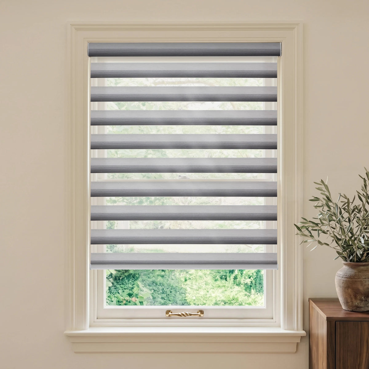 Gradient Grey Silver motorized room-darkening zebra blind in a bright room beside a wooden table and olive branches.