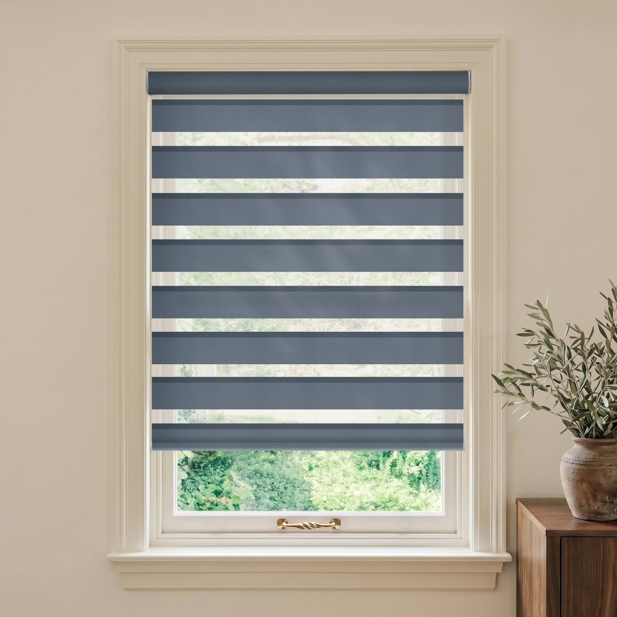 Luxury Blue Grey motorized room-darkening zebra blind in a cream room beside a wooden table and olive branches.