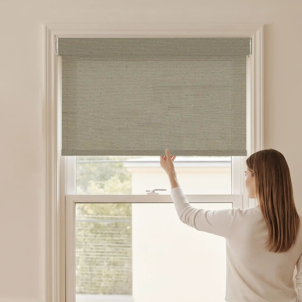 Woman adjusting a Graywind light filtering manual-motorized roller shade in Horizon (Sand) fabric.