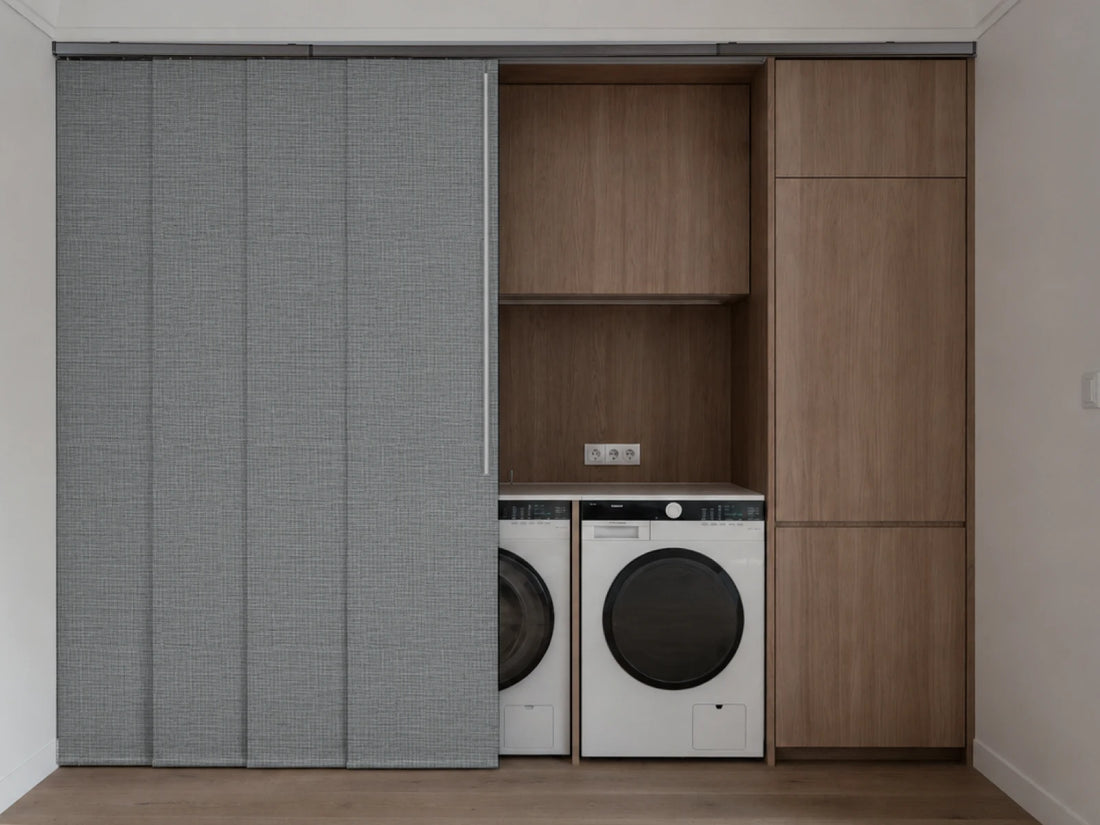 A modern built-in laundry nook with a gray textured sliding door on the left, open wood shelving in the center, and wood cabinet doors on the right, housing a white front-loading washing machine and a white dryer.