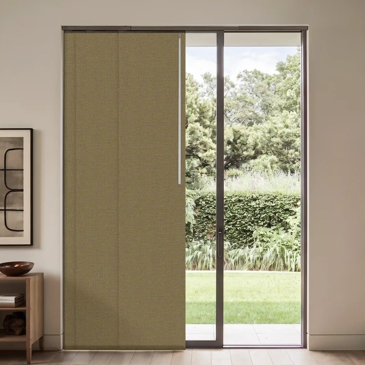 A sliding door panel system with a textured olive green fabric cover partially slid to the left, set in a modern room with a view of a green garden outside.