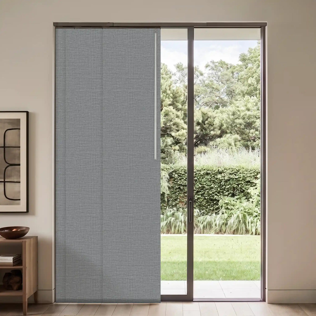 A gray textured sliding patio door panel installed in a modern sliding glass door, with a green garden visible outside and a beige interior wall on the left.