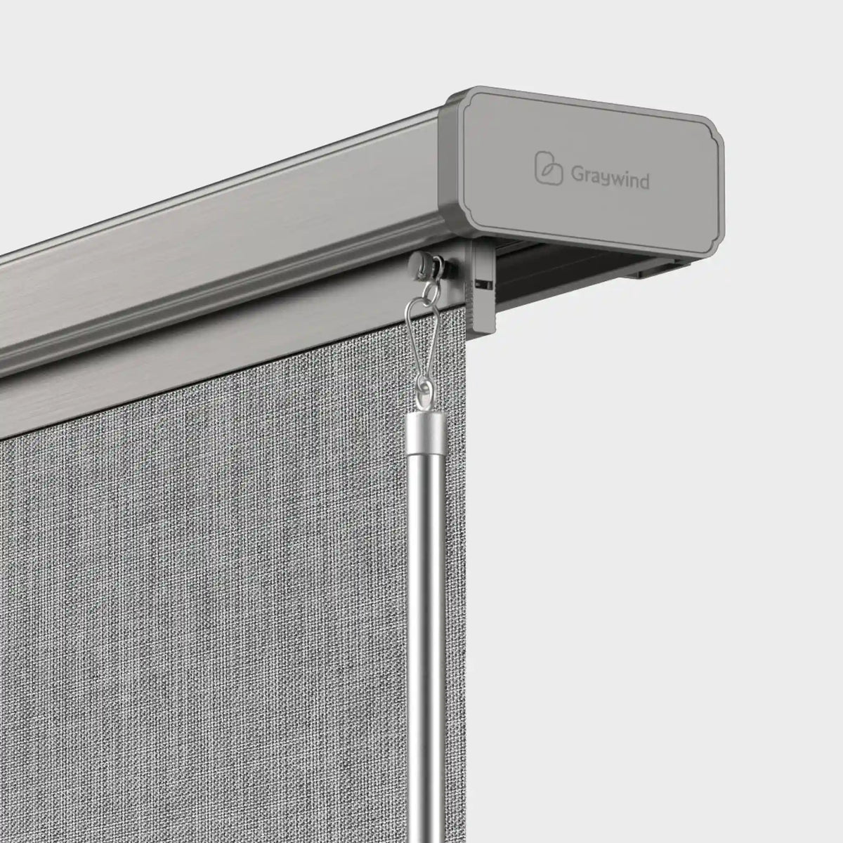 Close-up of a Graywind retractable outdoor roller shade system showing the gray metal header, fabric roller cover, hanging pole, and textured gray fabric curtain against a light gray background.