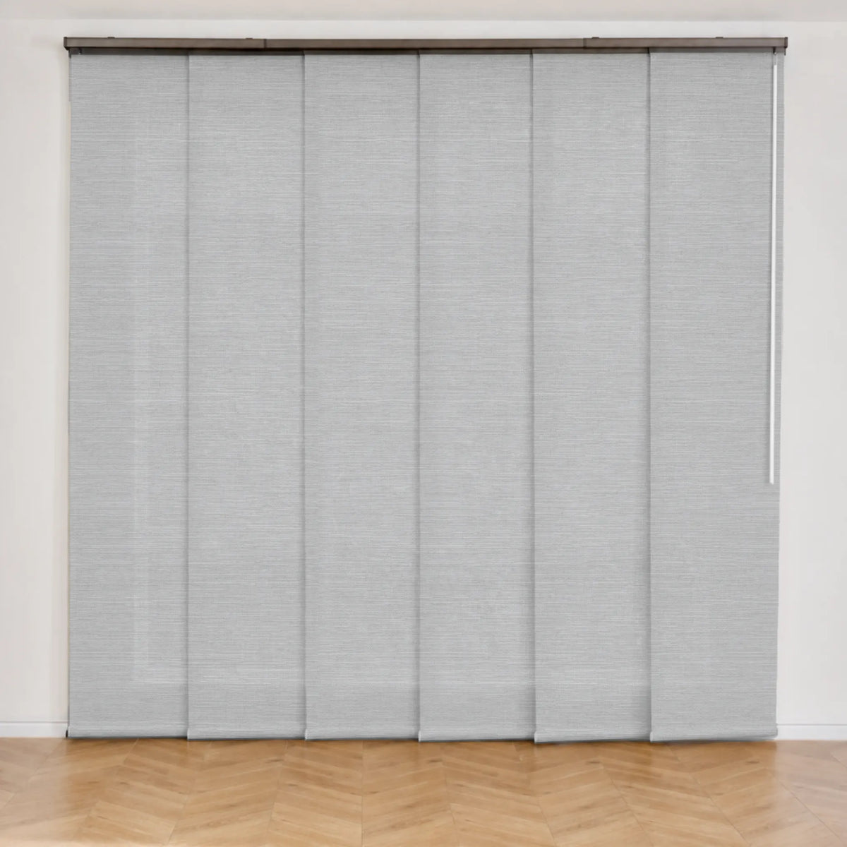 Light gray roller blind panels with a textured fabric surface, mounted on a rod over a window in a room with a light wood herringbone floor.