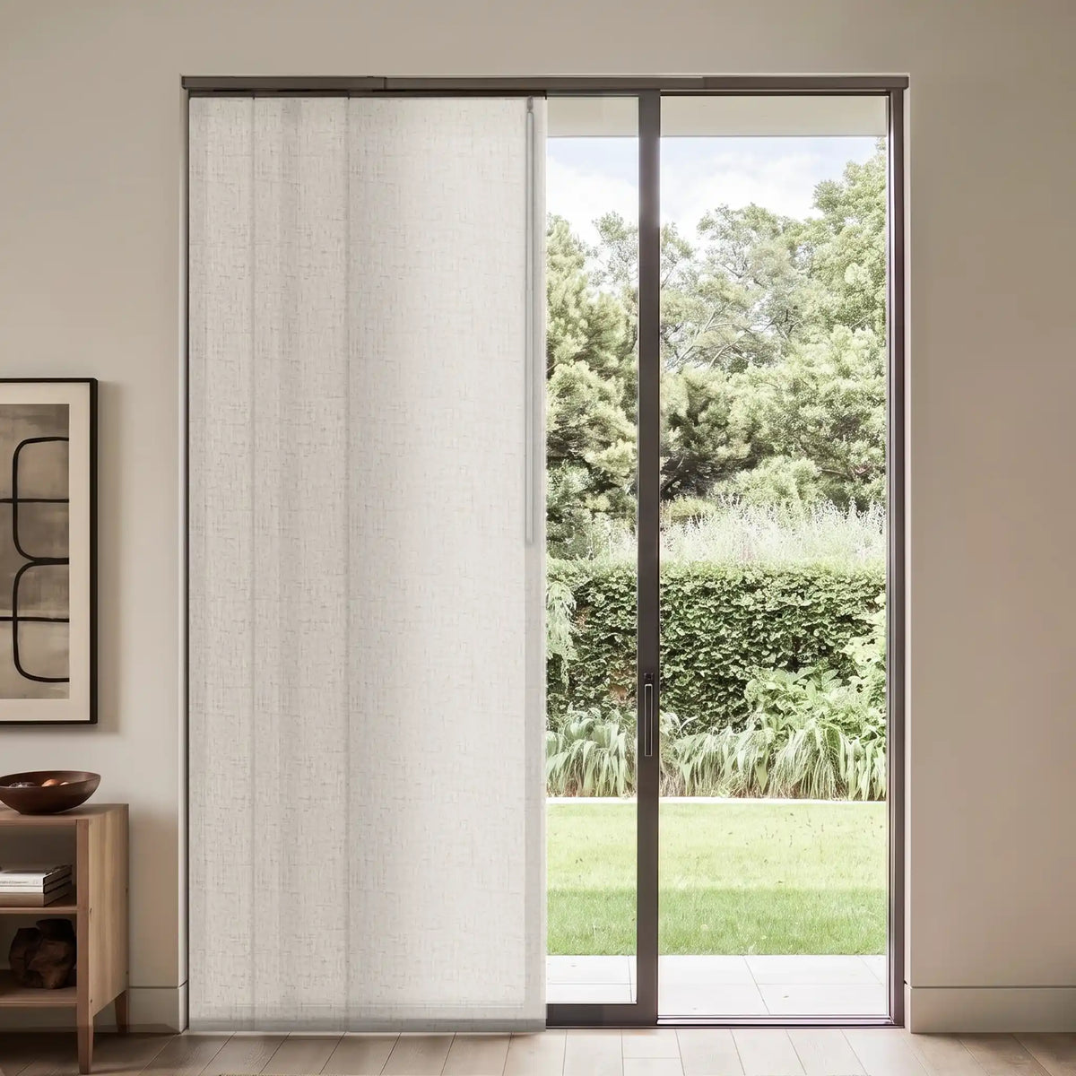 A tall, floor-length sheer white roller shade panel hanging on a sliding glass door in a modern room, with a garden visible outside.