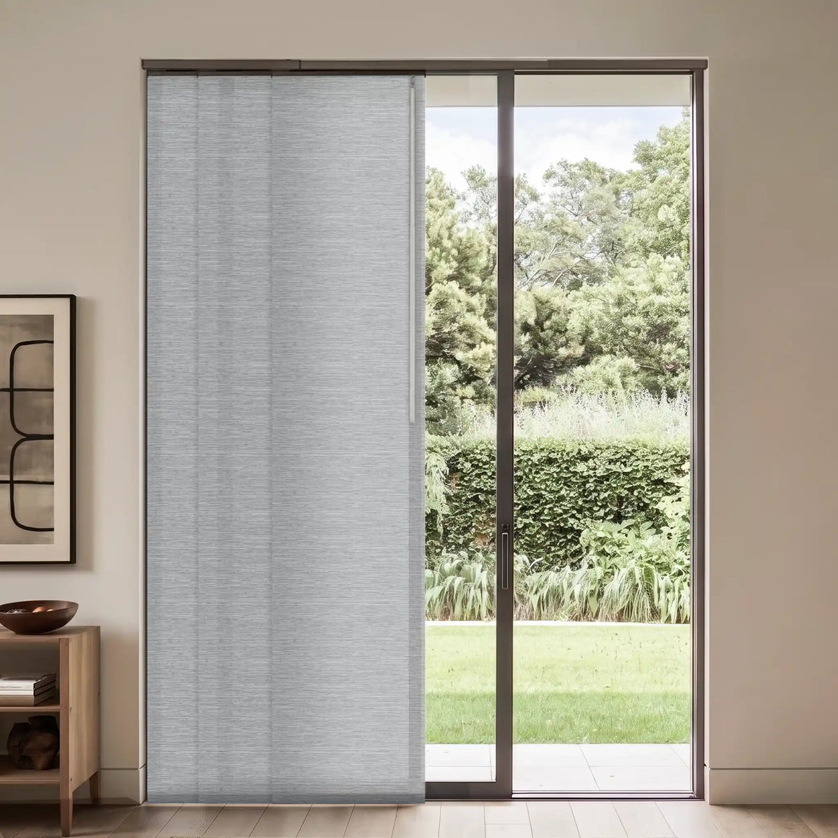 A light gray textured roller blind partially drawn over a sliding glass door, showing a garden view outside in a modern room setting.