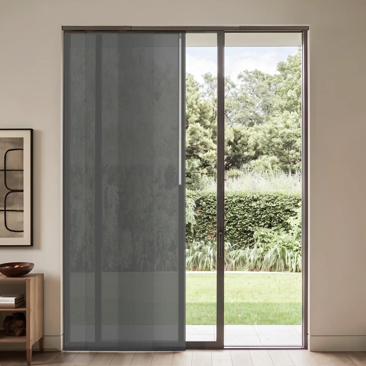 A modern sliding glass door with a dark gray sheer mesh screen panel on the left, set in a minimalist room with a light wood floor and a garden view outside.