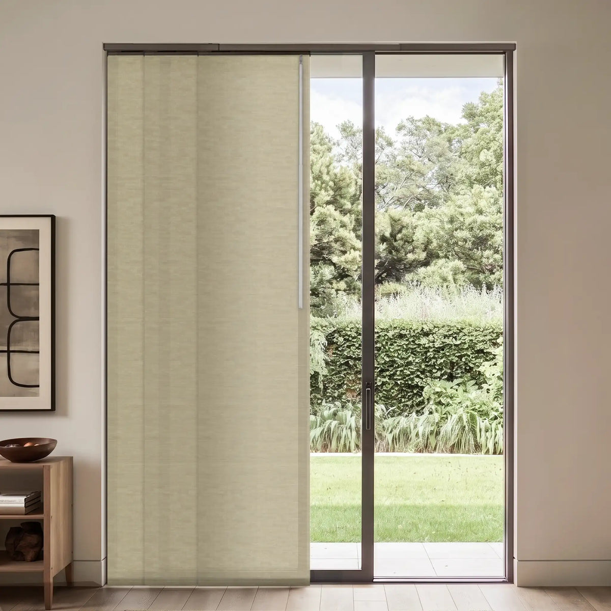 A light beige textured roller shade partially drawn over a sliding glass door, with a view of a green garden outside and a modern interior room on the left.