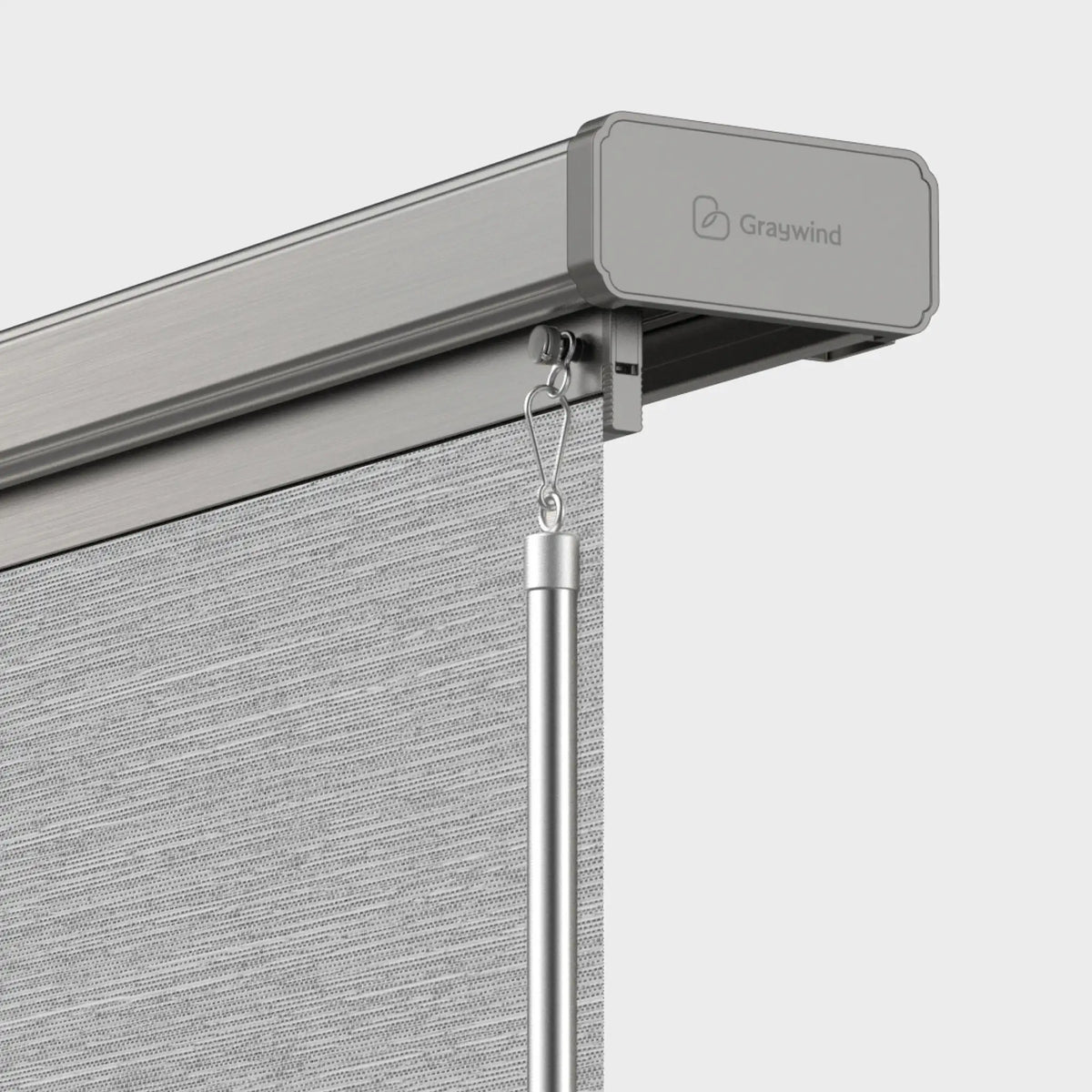 Close-up of a Graywind retractable roller blind system showing the gray fabric roller header, metal hanging hardware, and part of the textured gray blind on a light gray background.