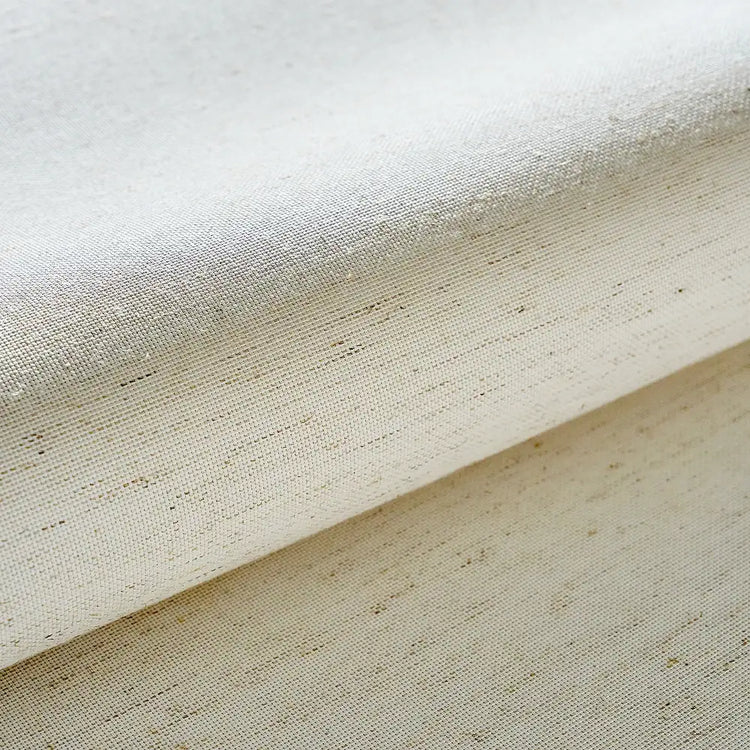 A close-up of a folded cream-colored woven fabric with a visible linen-like texture and subtle brown flecks, set against a matching background.