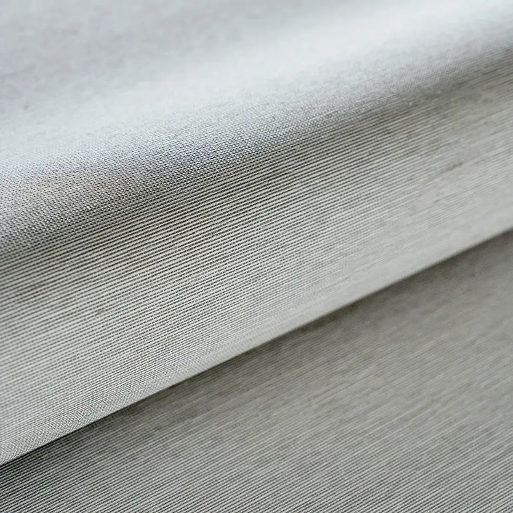 A close-up of light gray ribbed fabric with a fine textured weave, folded diagonally across the frame.