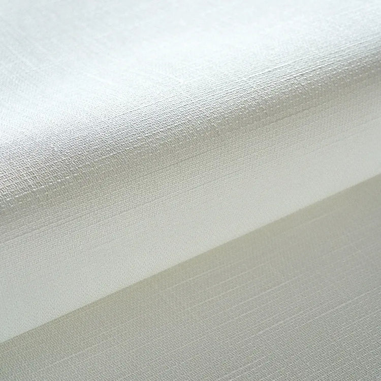 A close-up of a white textured fabric, likely wallpaper or a decorative wall covering, showing a fine linen-like weave and a folded corner.