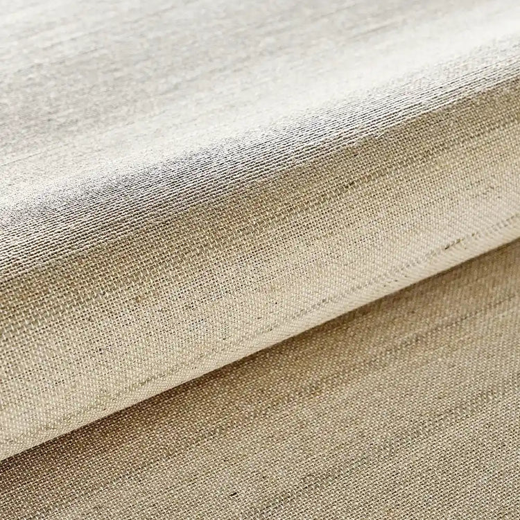 A close-up of a woven fabric with a textured linen-like surface in a warm beige color, folded to show the weave and drape.