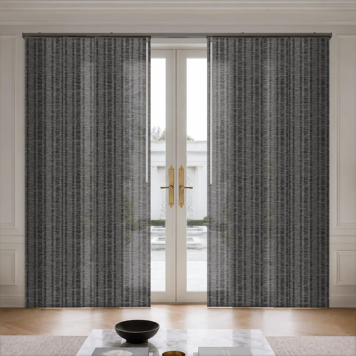 A pair of gray textured window curtains hanging on either side of a white French door in a bright, modern room with light wood floors and a marble coffee table.