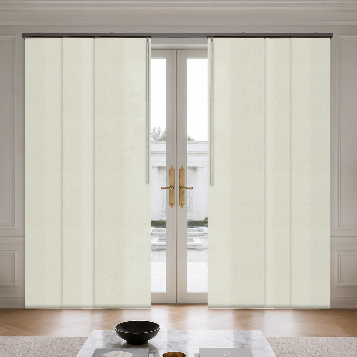 A pair of cream-colored, vertically pleated sliding patio curtains shown installed on a track system flanking a set of double glass doors in a bright, modern room.