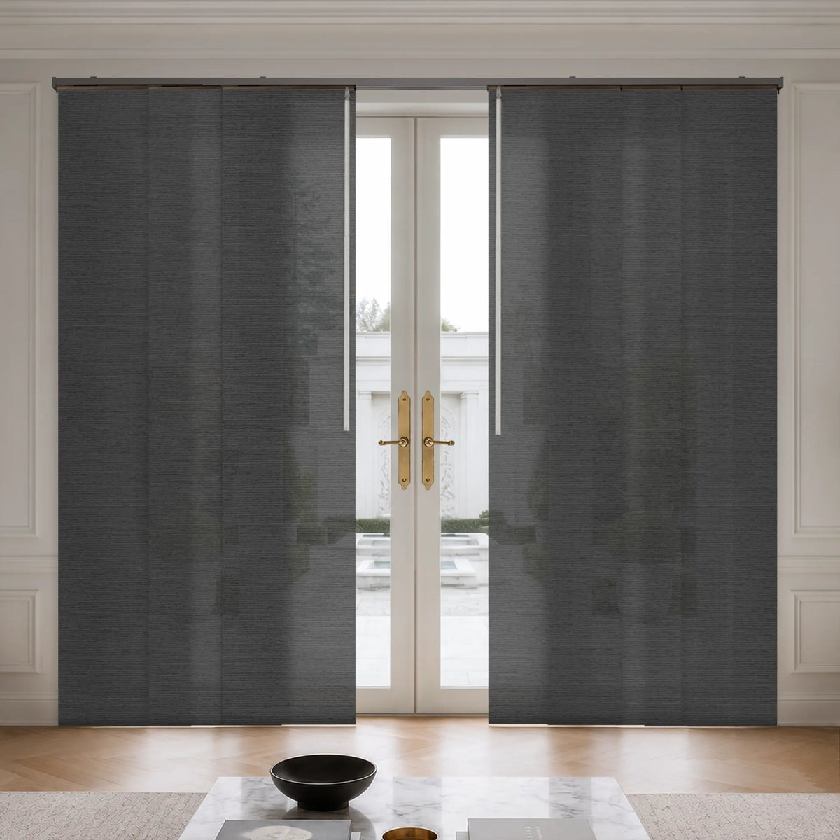 Dark gray textured roller blind panels partially drawn over a set of white double glass doors in a bright room with light wood flooring and white wall molding.