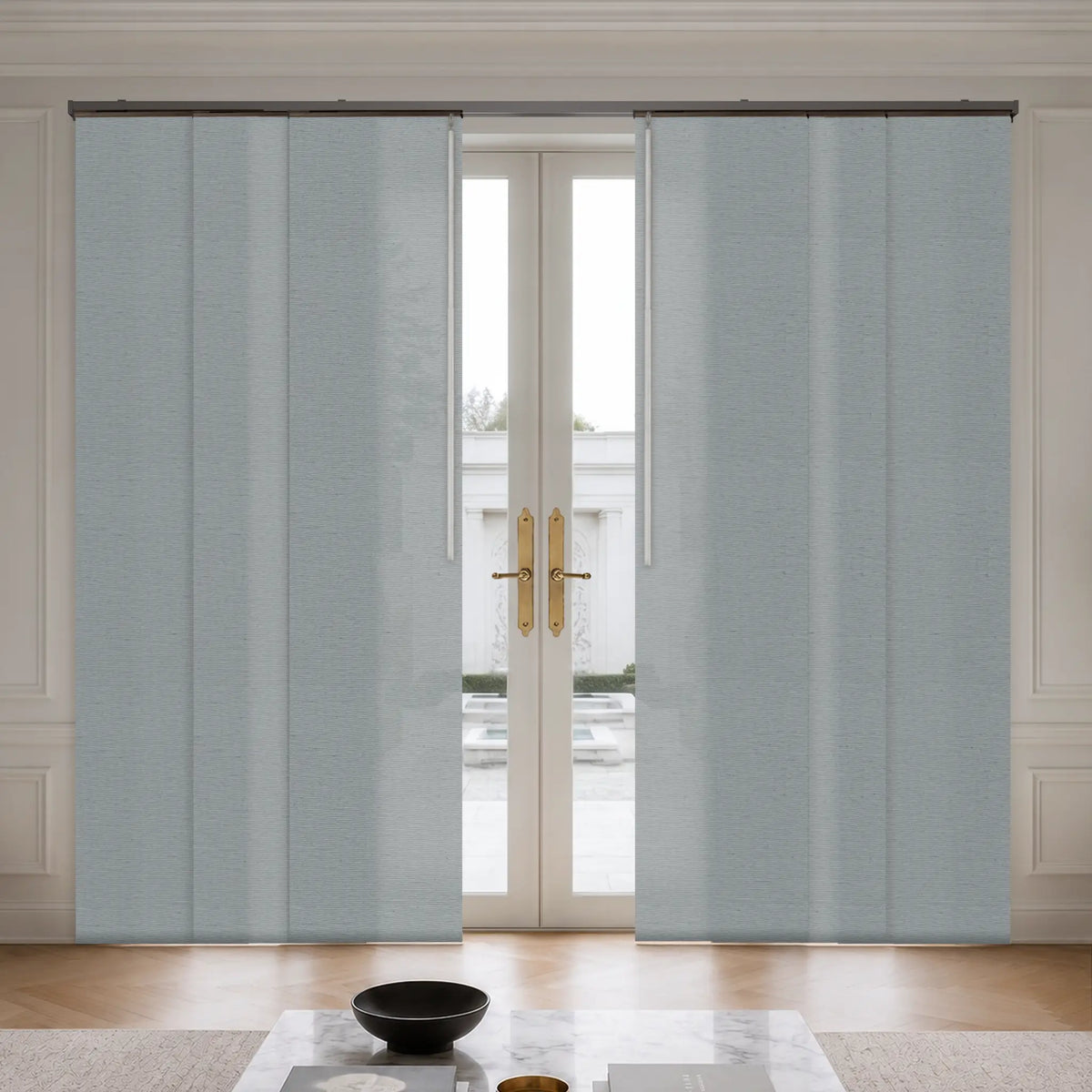Light blue textured panel doors or curtains installed on a double glass door in a bright, modern interior room with wood flooring and a marble coffee table.