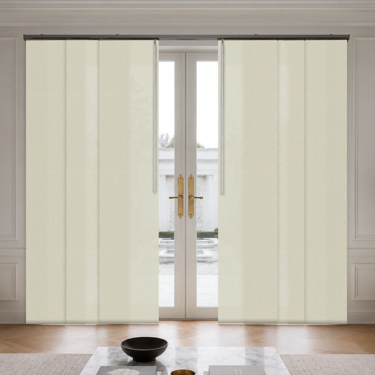 A pair of cream-colored, vertically pleated roller blind curtains hanging on a black rod over double glass doors in a bright, modern room.