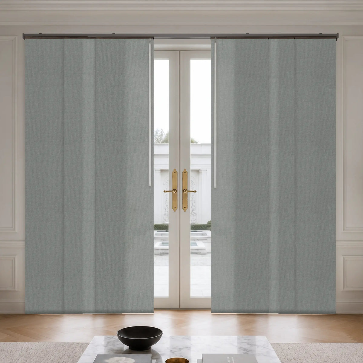 A pair of light gray textured rollerback patio curtains hanging on a black metal rod over a set of double glass doors in a bright, modern room.